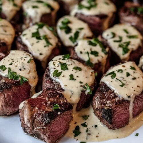 Garlic Butter Steak Bites coated in creamy Parmesan sauce, garnished with parsley, served on a rustic plate.