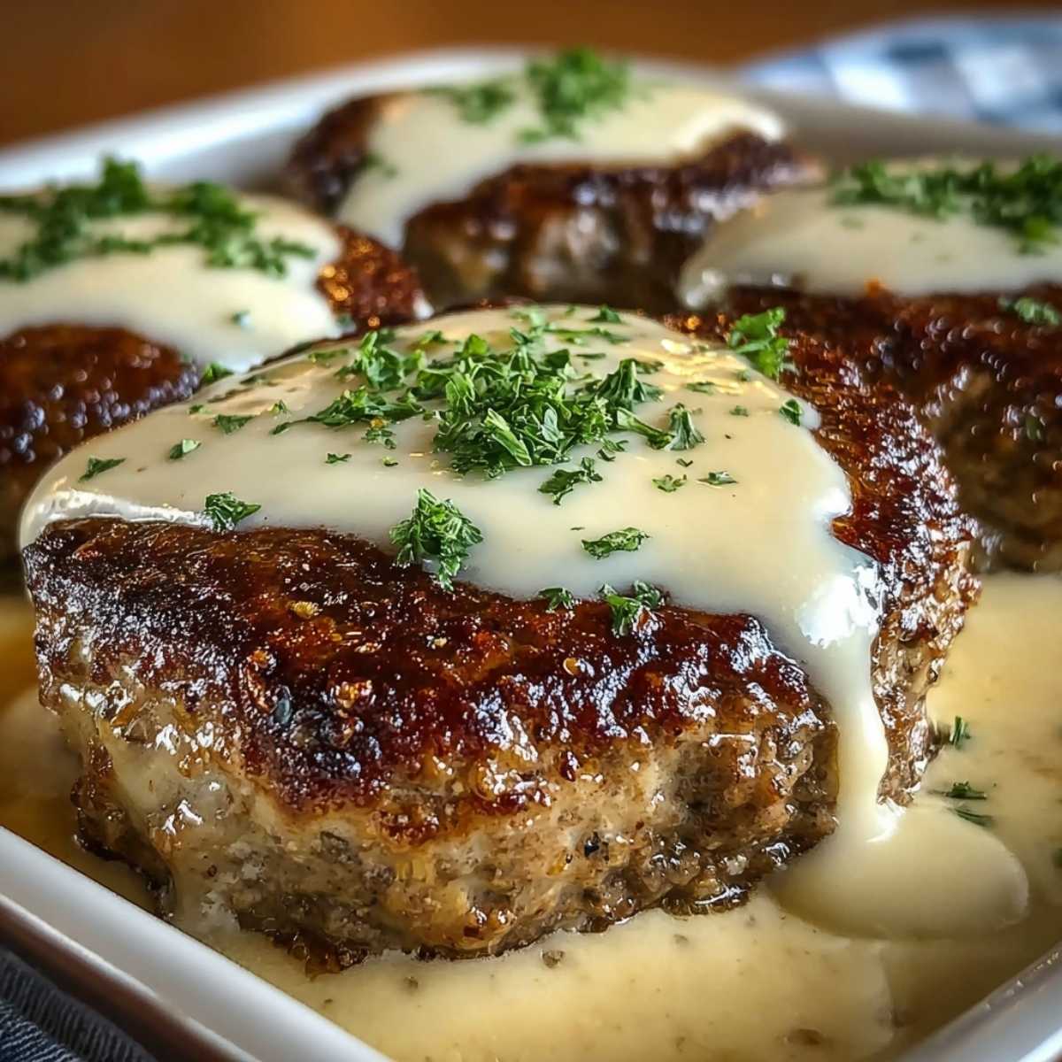 Amish Hamburger Steak Bake with rich white gravy and fresh parsley on a modern white serving dish, ready to eat