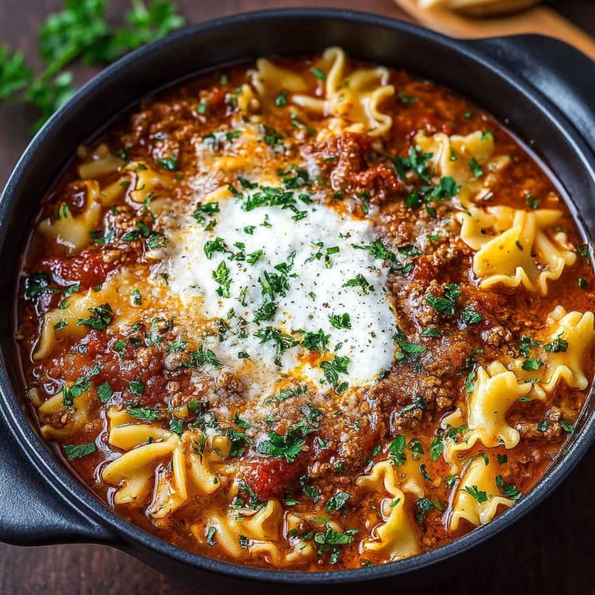 Overhead view of a bowl of Easy Lasagna Soup, shown here made with bowtie pasta as a variation, garnished with grated Parmesan cheese and fresh chopped parsley