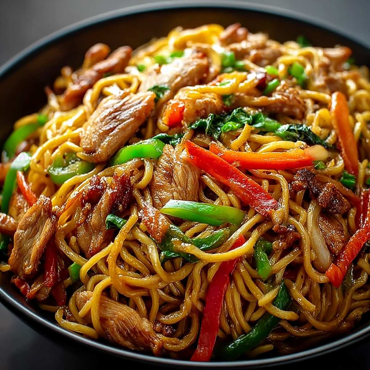 Chicken Lo Mein recipe in a dark bowl, showcasing glossy egg noodles, sliced chicken breast, bell peppers, and scallions.