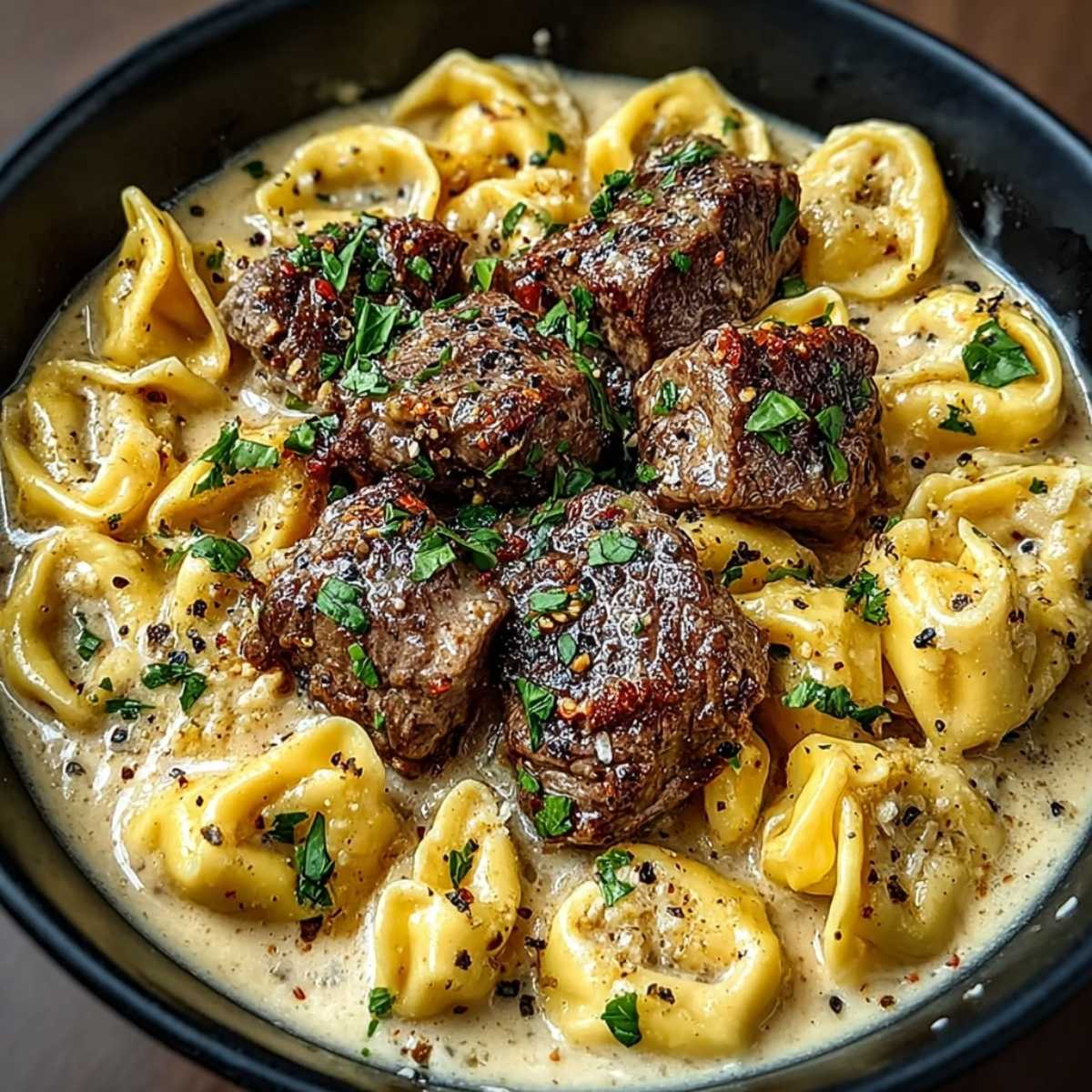 Cracked garlic steak tortellini in a skillet with seared steak bites, cheese tortellini, creamy garlic sauce, parsley, and cracked pepper.