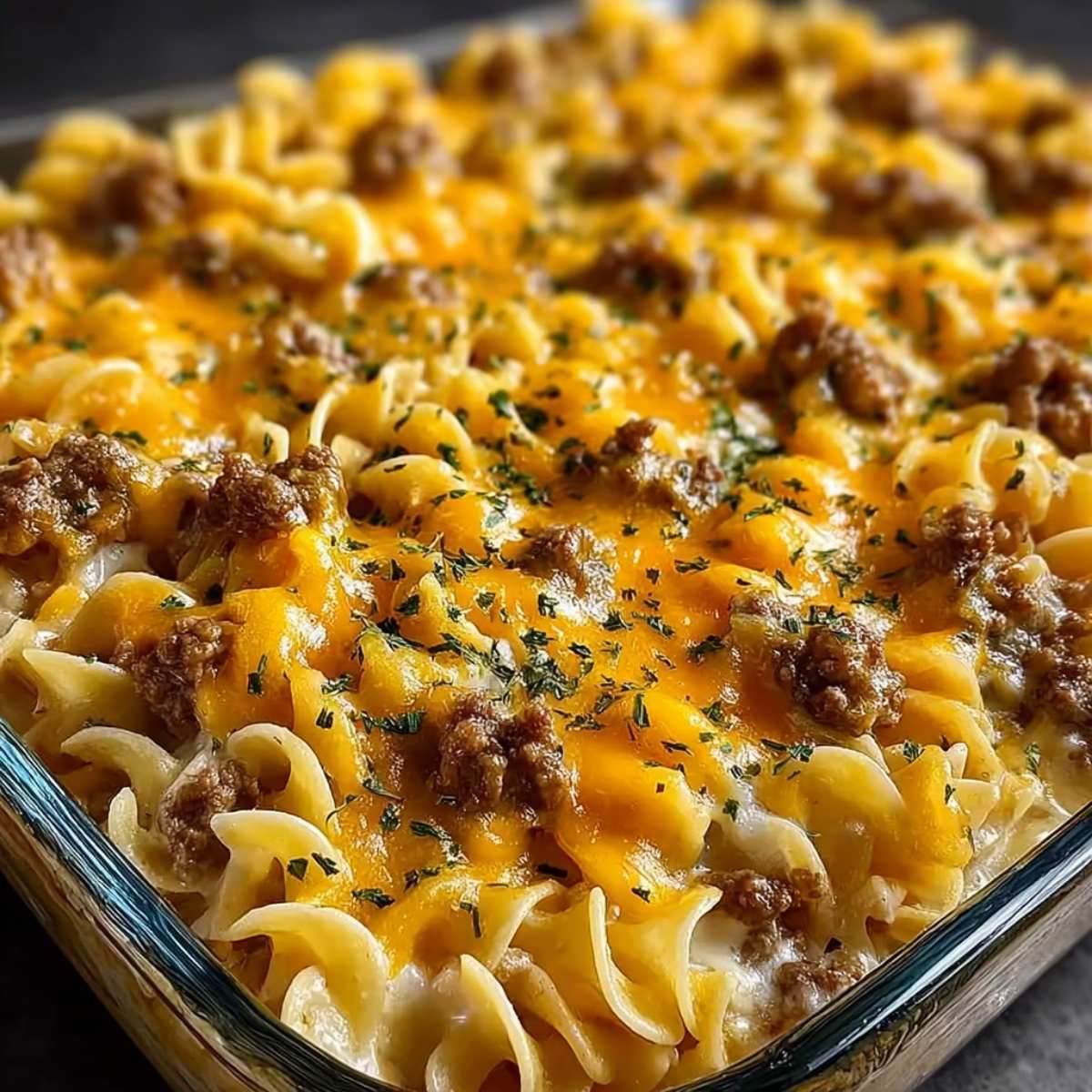 Sour cream beef noodle casserole in a glass baking dish, showing creamy egg noodles, melted cheddar cheese, and seasoned ground beef.