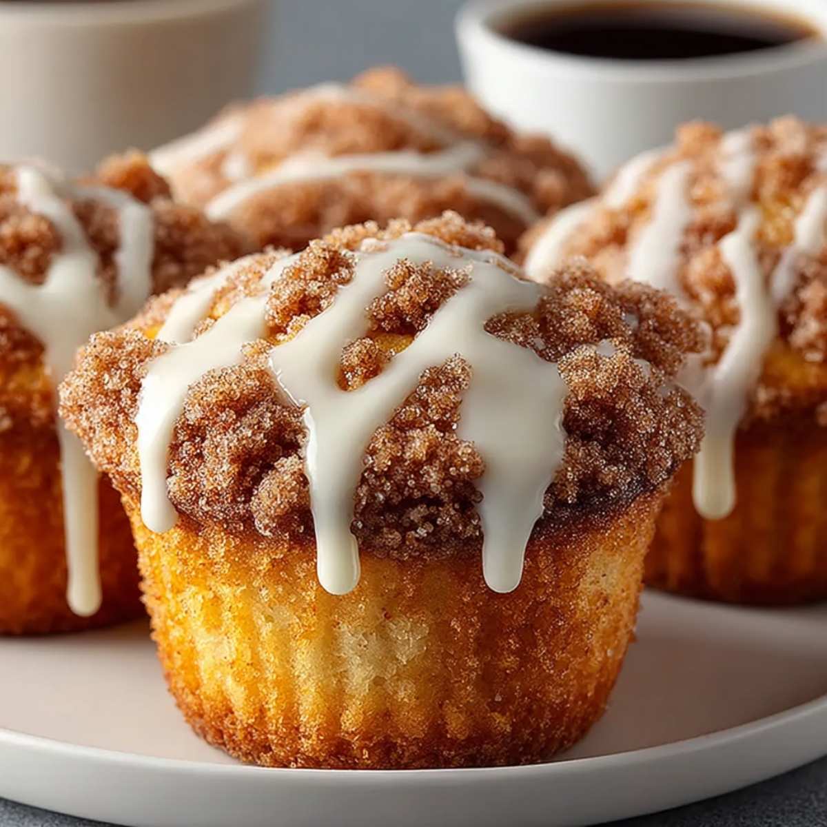 Coffee cake muffins with cinnamon crumb topping and vanilla glaze on a white plate, showing golden bakery-style texture.