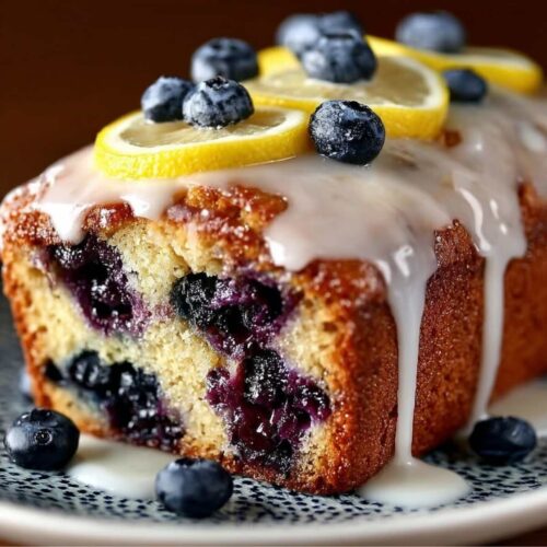 Easy Lemon Blueberry Loaf 9 Lemon Blueberry Loaf on a ceramic plate, showcasing moist crumb with juicy blueberries, topped with lemon glaze and fresh lemon slices.
